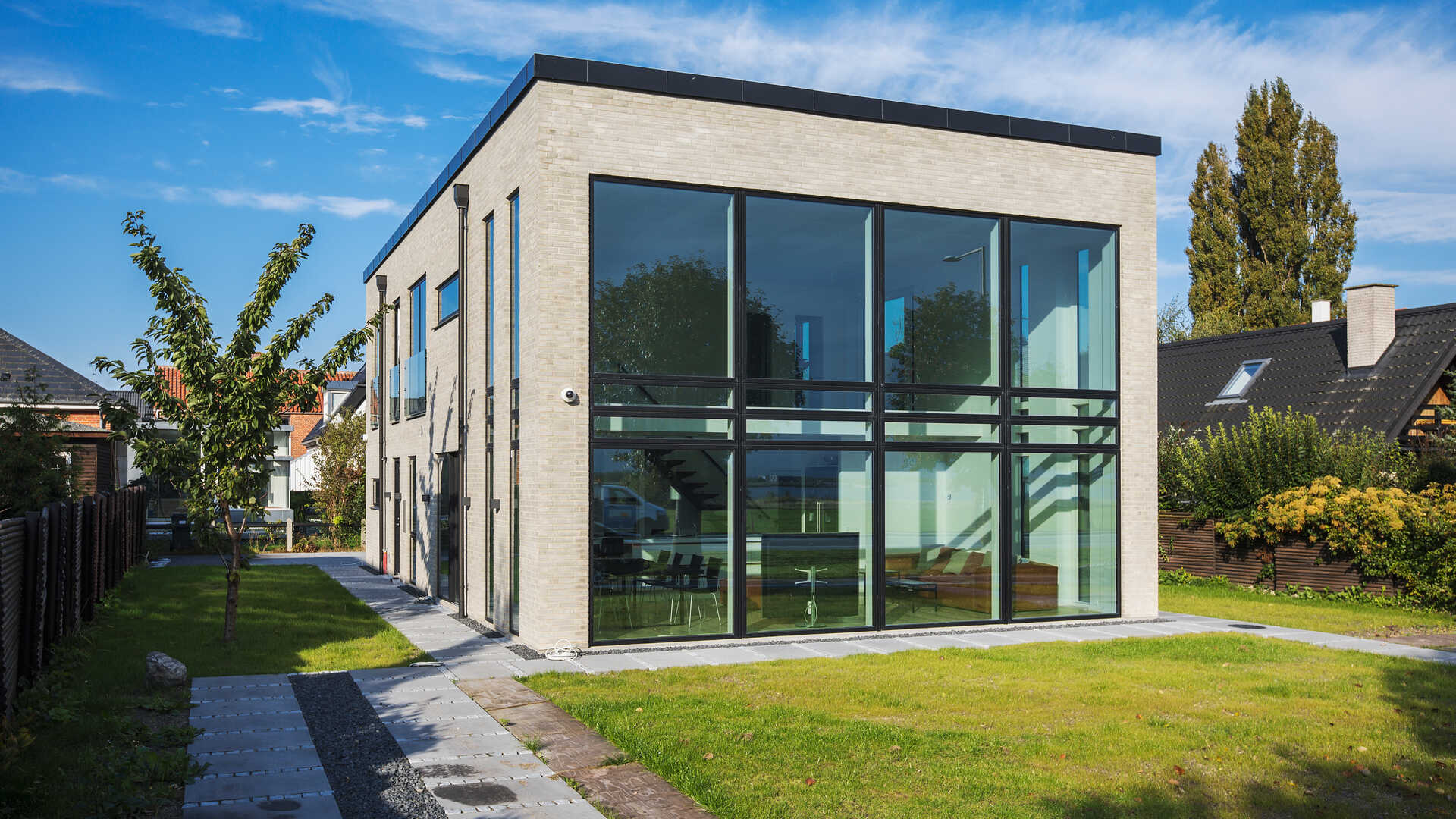 Palæarkitektur opført i moderne og industrielt inspireret stil. Villaen har store, høje vinduer, fladt tag og gyldengrå facadesten.