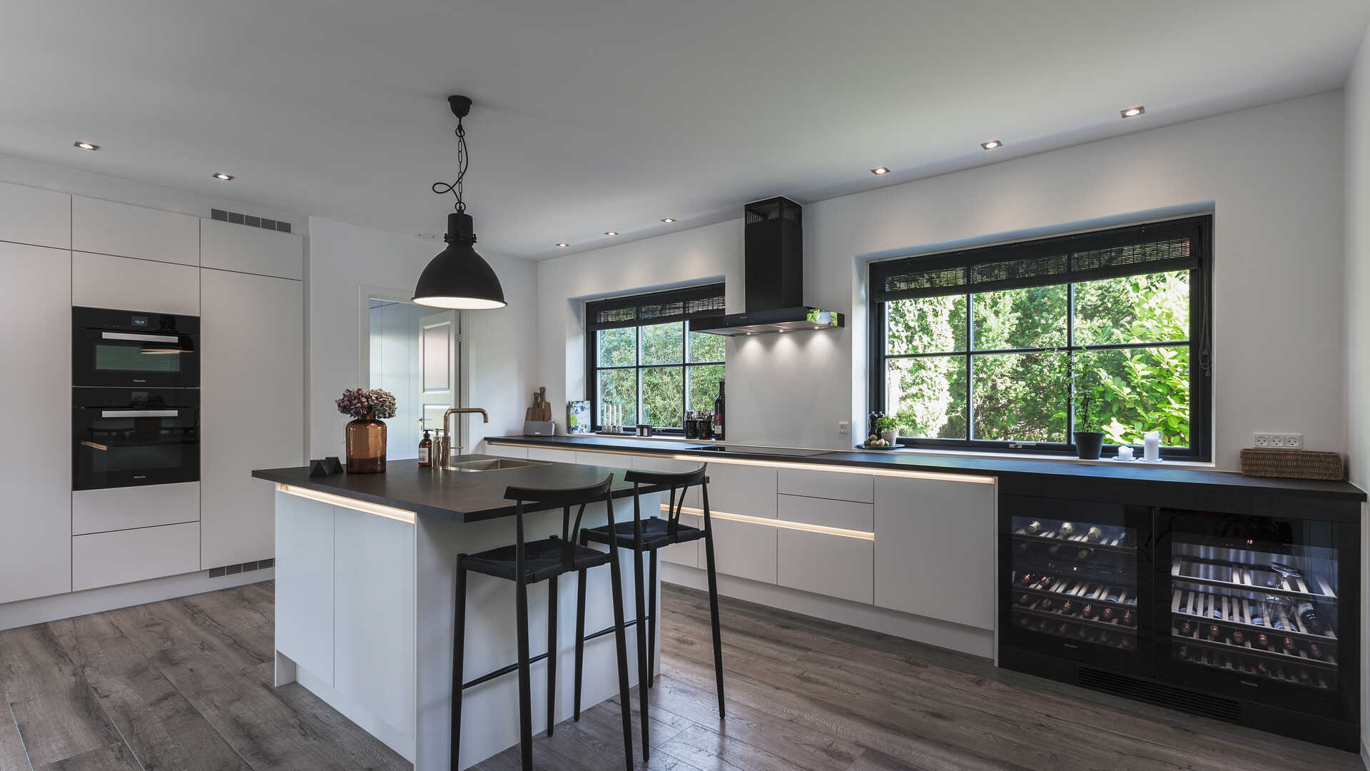 Imponerende køkkendrøm med plads til vin, hygge og masser af madlavning. De hvide elementer er grebsløst design fra HTH, og matcher lækkert den industrielle  stil, der gennemsyrer huset. Bemærk også flotte trægulve, indbygningsspots og den store skabsvæg.